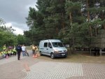 Radiowóz nieoznakowany, obok grupa osób w kamizelkach odblaskowych oraz policjant.